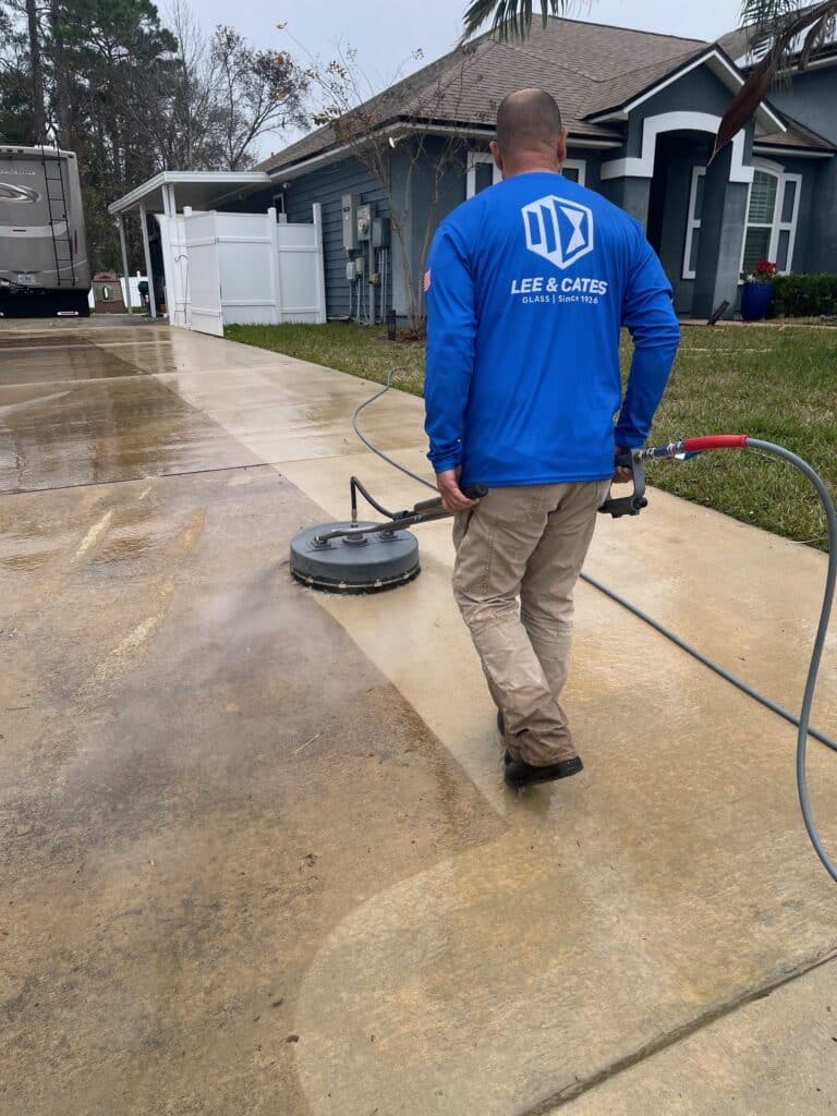 Technician pressure washing a residential paver driveway using a surface cleaner outside a home in Jacksonville, FL, removing dirt and grime with visible steam.