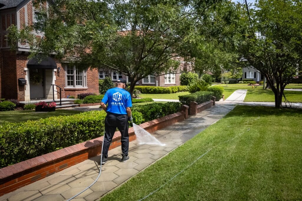 Technician pressure washing a concrete walkway along a front yard in a Jacksonville neighborhood to remove grime and enhance curb appeal.