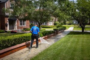 Technician pressure washing a concrete walkway along a front yard in a Jacksonville neighborhood to remove grime and enhance curb appeal.