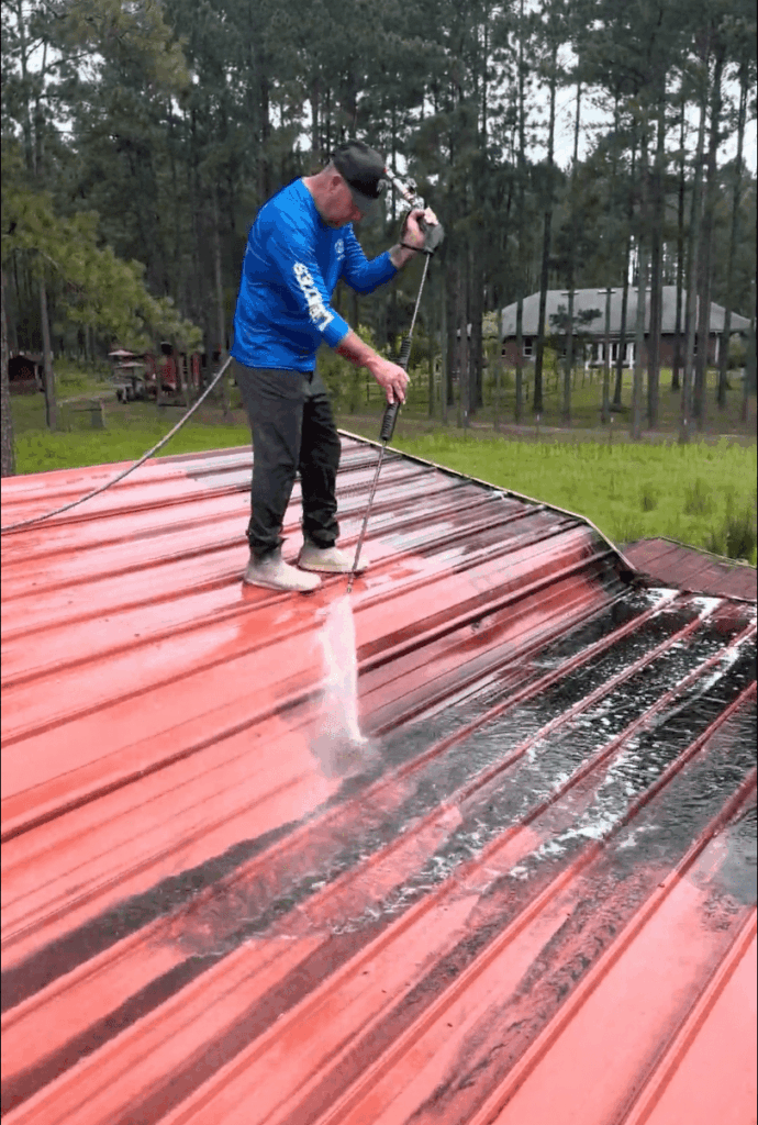 Commercial roof being pressure washed by Surface CPR technician, showing clean water line.