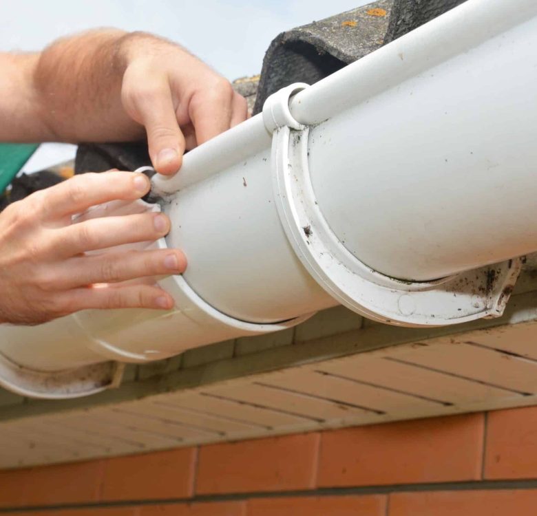 A man is installing, repairing a roof gutter, fitting union bracket and screwing it to the fascia.
